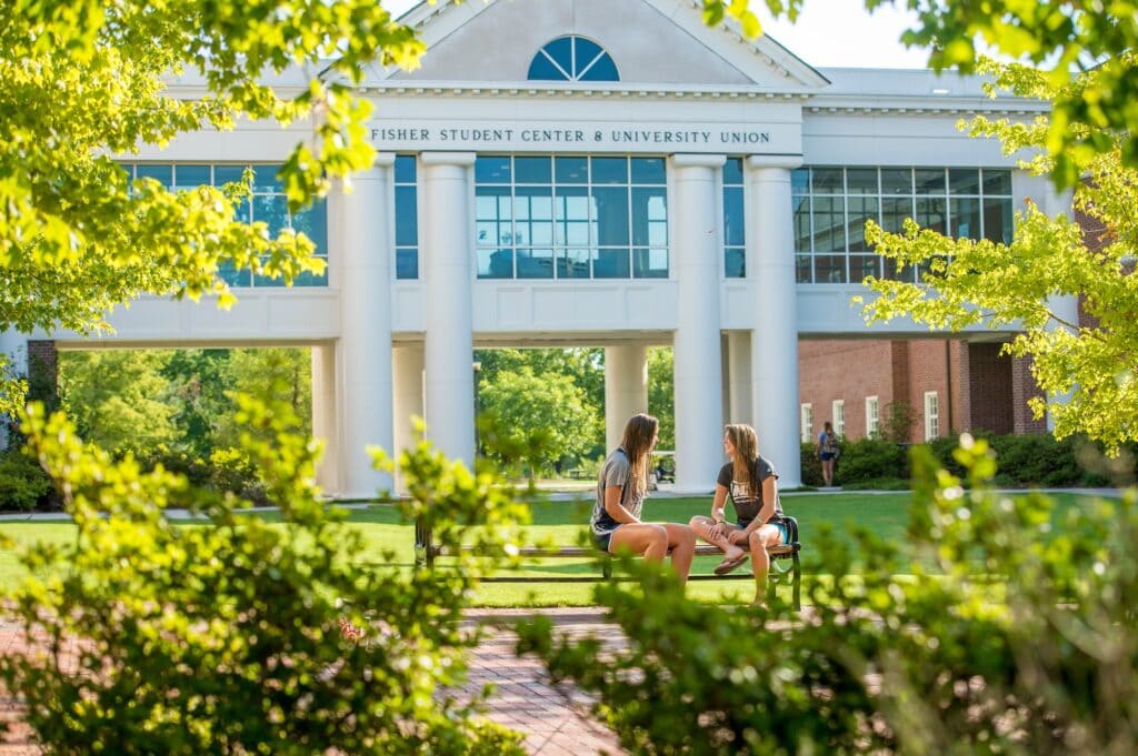 Internationale Studentinnen sitzen auf einem US-Campus und unterhalten sich.